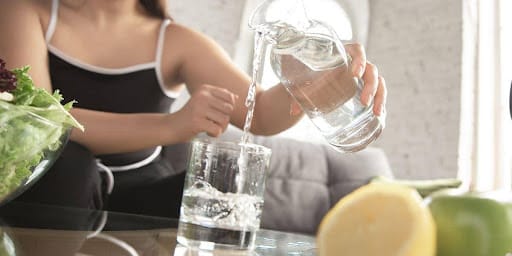 Mulher colocando a água da garrafa no copo